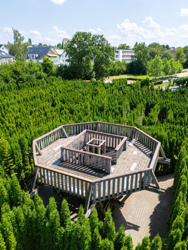 Holz-Aussichtsplattform im Irrgarten aus schräger Drohnenperspektive mit Blick auf umliegende Häuser