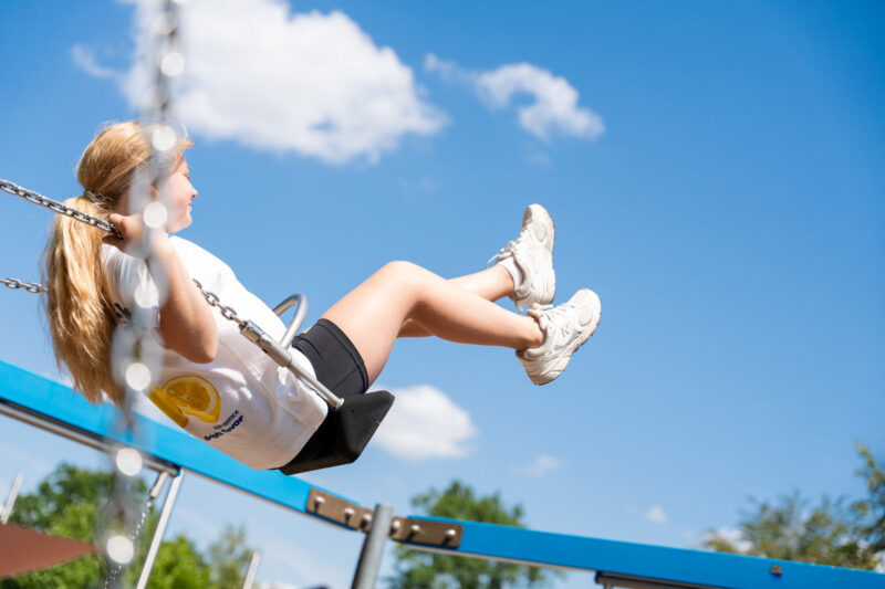 Mädchen schwingt auf einer Schaukel hoch in den blauen Sommerhimmel