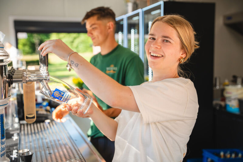 Zwei lächelnde Barkeeper zapfen frisches Augustiner-Bier an der Theke der Strandbar von Webers Garten am Kurparksee