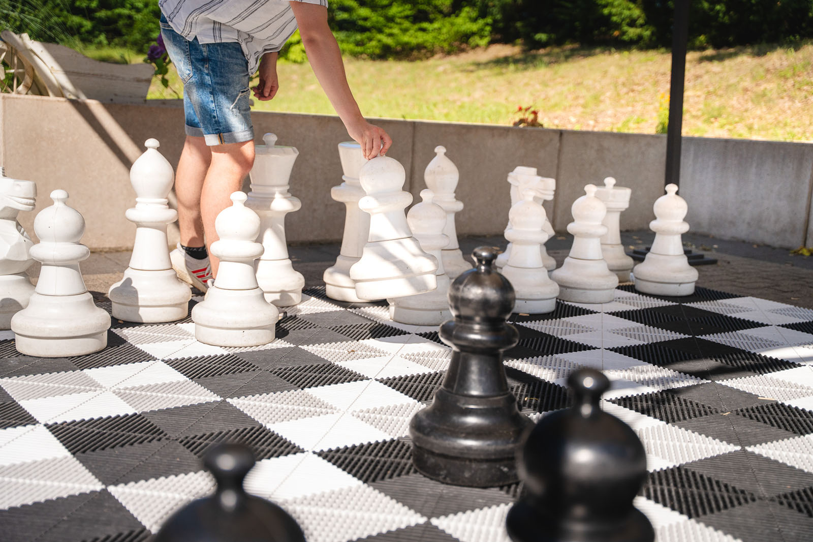 Kind spielt Riesenschach mit großen schwarz-weißen Schachfiguren auf dem Außenschachfeld bei Webers Garten am Kurparksee